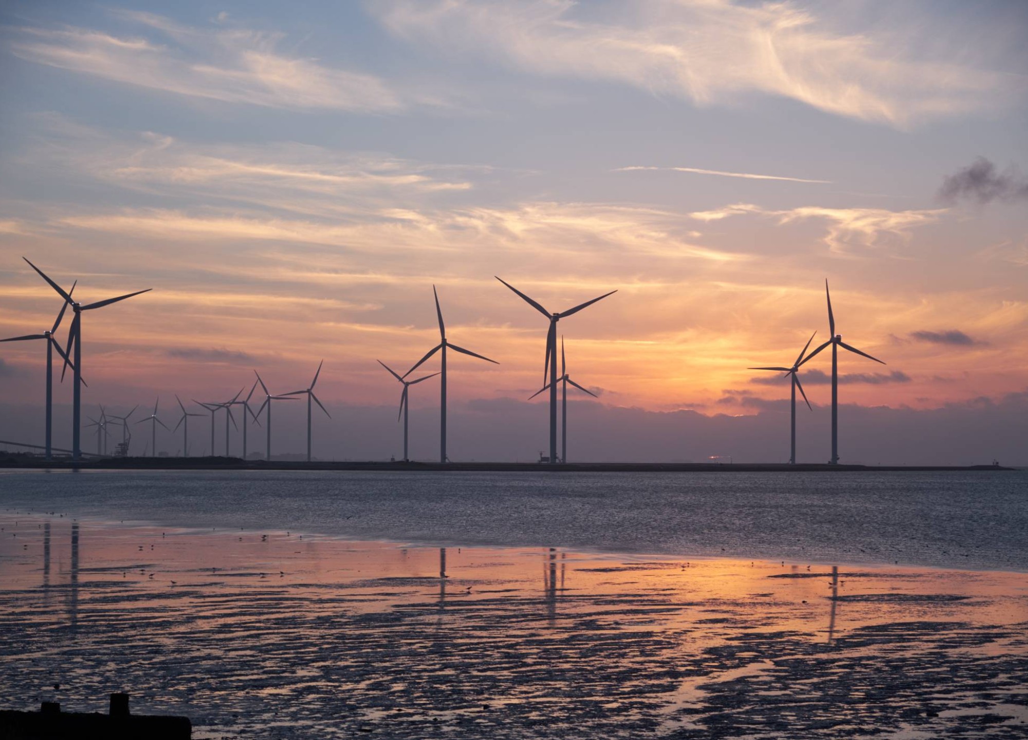 Windmolens bij ondergaande zon in zee
