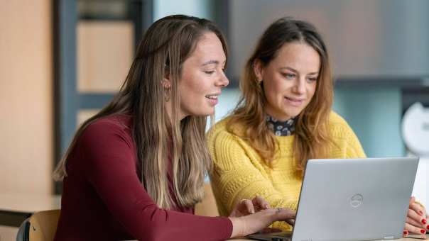 2 cursisten Basisvaardigheden in het Mbo overleggen in een klas bij een laptop.