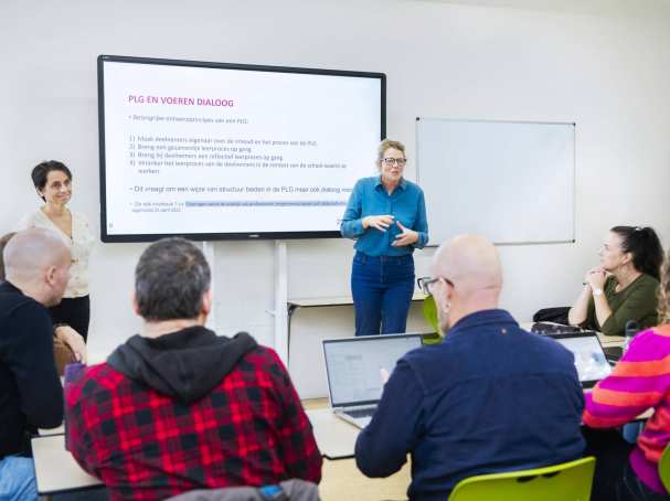 Twee vrouwelijke docenten staan enthousiast uit te leggen voor de klas, terwijl de studenten aandachtig luisteren