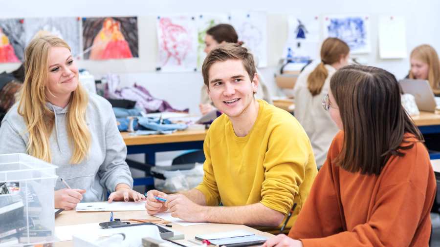 Fotoshoot maakdagen beeldende vorming 2022.Drie studenten met elkaar in overkeg tijdens de les beeldende vorming. De jongen in het midden lacht