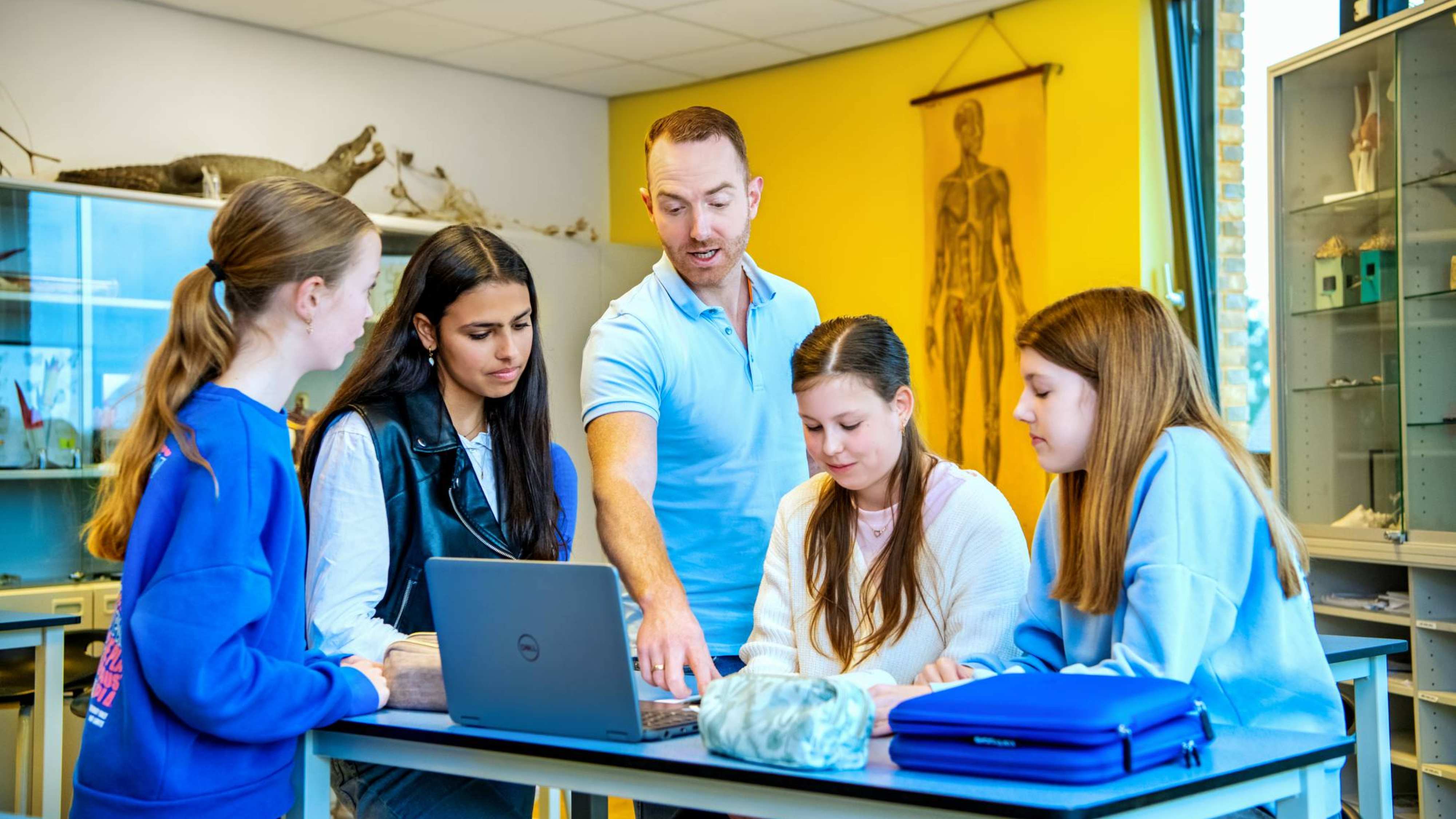 Docent Niels Janssen staat samen met 4 leerlingen rond tafel terwijl ze naar een laptop kijken op het Citadel College.