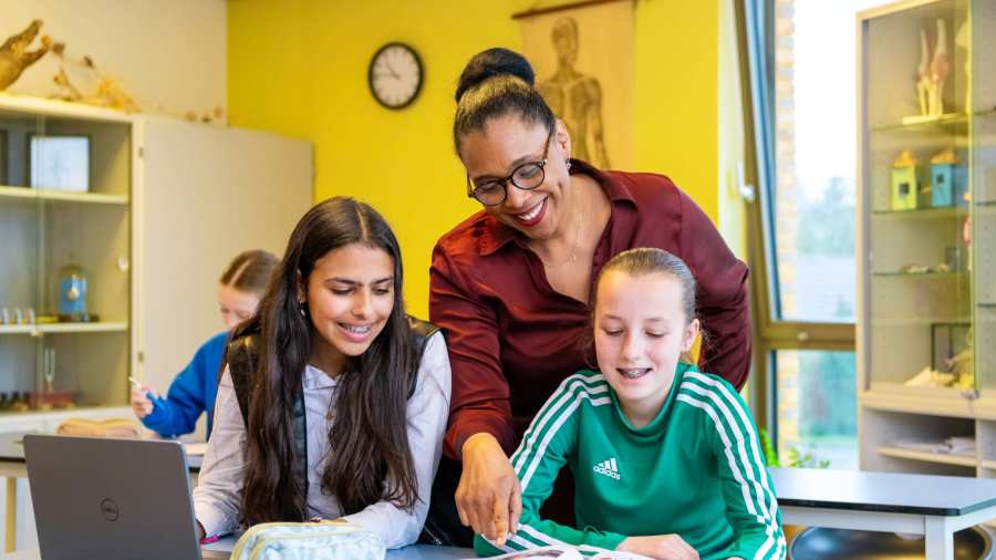 2 lachende leerlingen kijken naar een boek waar de docenten heen wijst op het Citadel College.