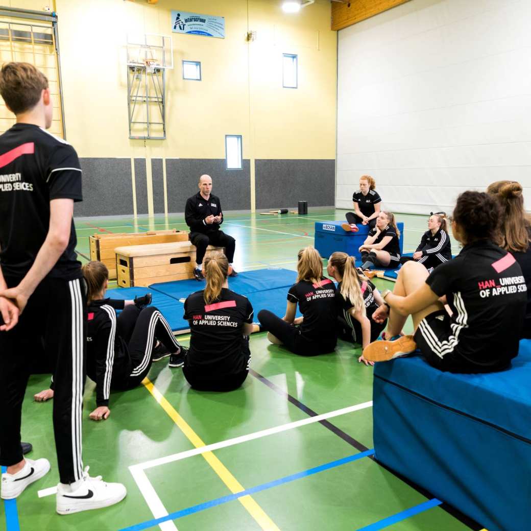 Pabo-ALO studenten zitten in de gymzaal rondom de docent die instructies geeft.