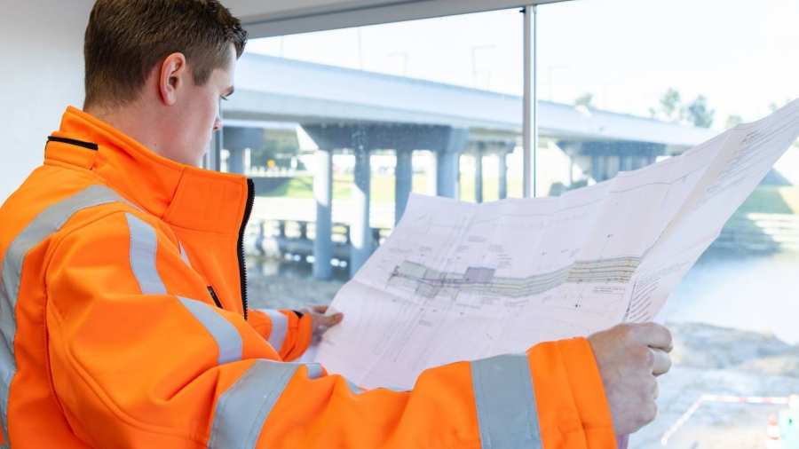Man in oranje werkjas checkt staand voor het venster van de bouwkeet de  werktekening
