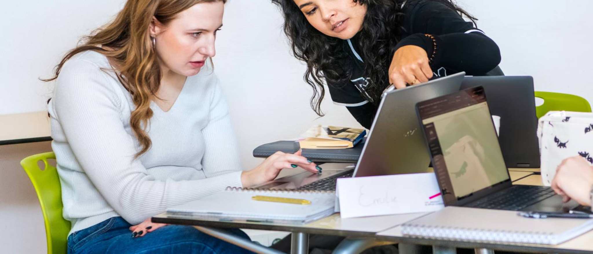 Twee studenten Leraar Engels kijken aandachtig naar de laptop en één student wijst naar het scherm.