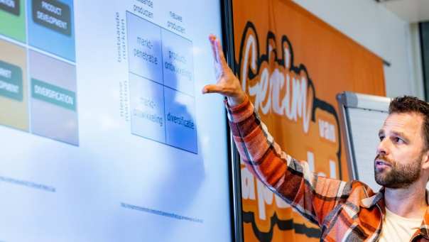 sportkunde deeltijd docent wijst aan op bord in klaslokaal 2024