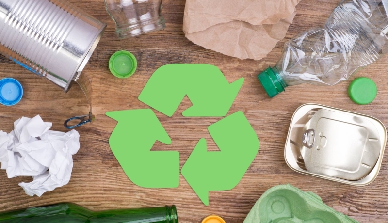 reclyvle teken met drie pijlen die elaar volgens en daaronder recyclebare spullen zoals blikjes en flessen en papier.