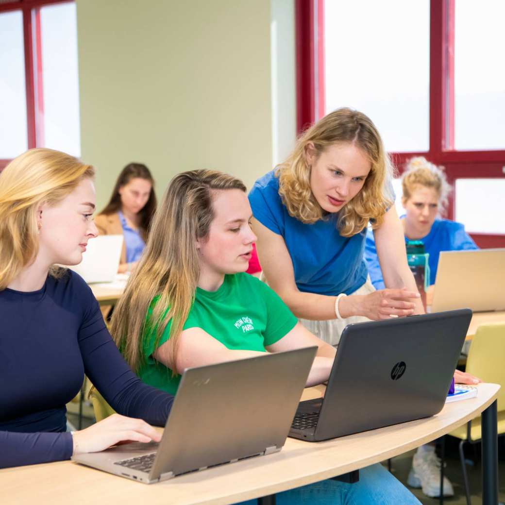 Docent Verpleegkunde geeft uitleg aan studenten achter de laptop