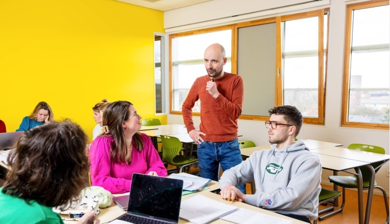 Lachende docent zit aan tafel bij haar studenten.