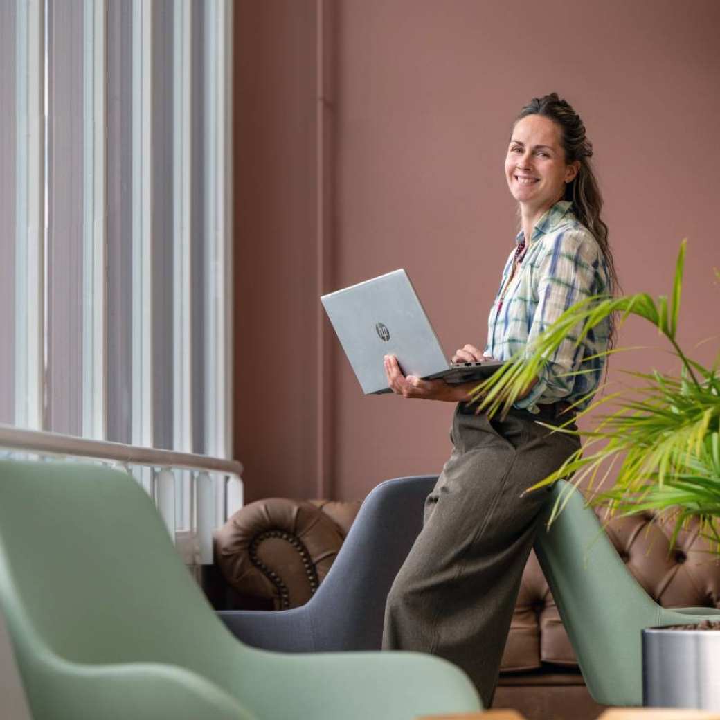 Masterstudent staat met laptop in handen op campus