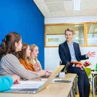 Duits docent bladert door studieboek en praat richting leerlingen