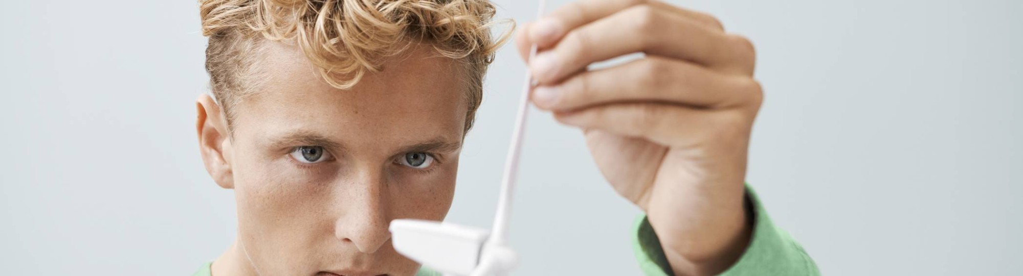 jongen met blonde haren met een groene trui aan die kijkt naar het model van een windmolen