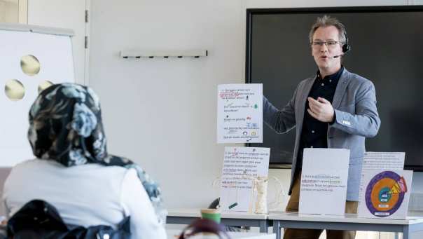 Man houdt presentatie en houdt hierbij ideeën op papier in de lucht voor de klas