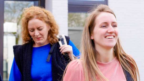 drie vrouwen komen naar buiten gelopen, roze trui is aan het lachen.