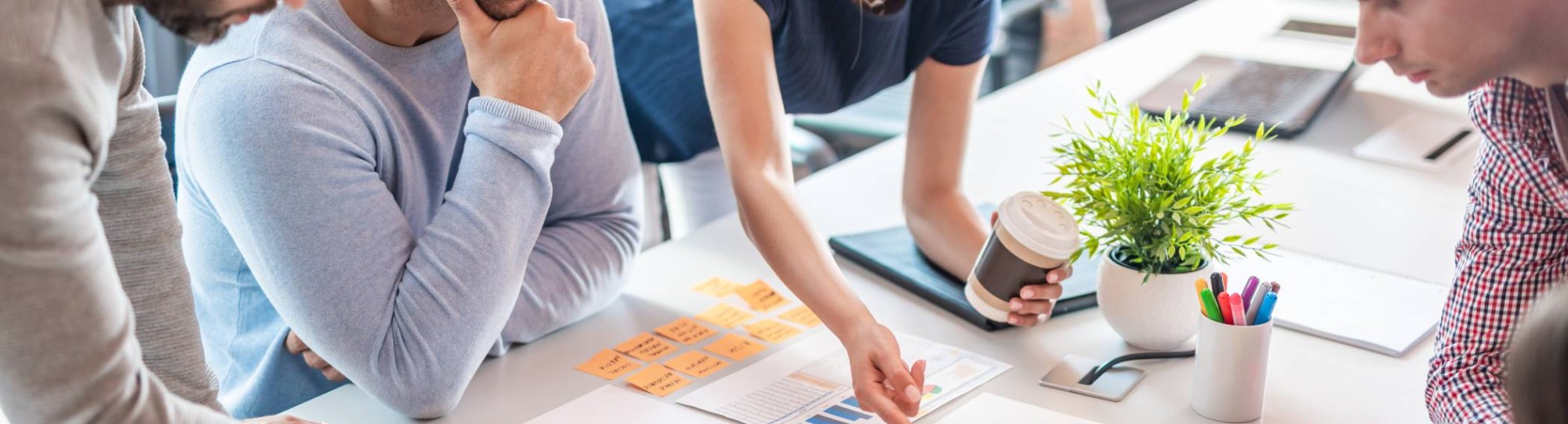 Sfeerbeeld van collega's die samenwerken aan een tafel met post-its, schema's en tabellen 