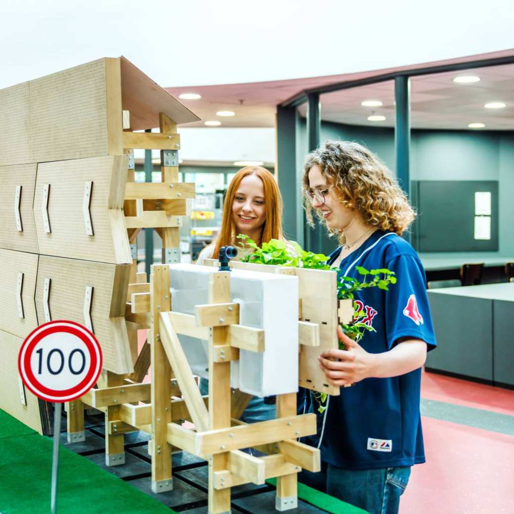 Op de foto zie je twee vrouewlijke studenten bij de InfraWall staan. Dit is een multifunctionele biobased en dus circulaire geluidswal die studenten van de HAN hebben ontworpen en gemaakt.