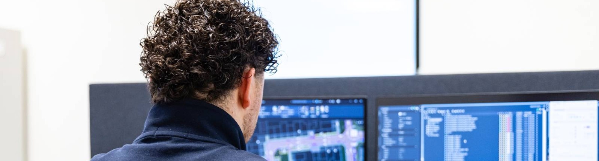 Man werkt op twee beeldschermen aan een bouwontwerp. Op de voorgrond staat een plant
