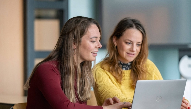 2 studenten kijken lachend samen naar een laptop.