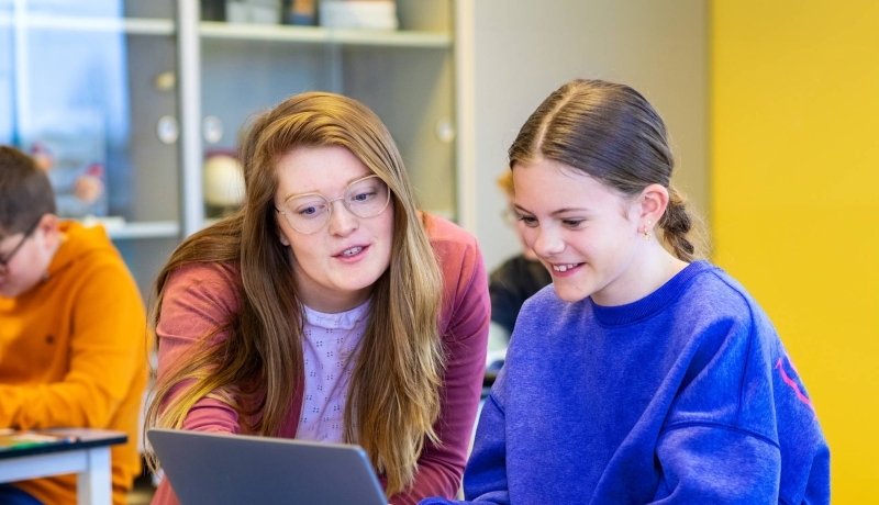 1 student aan de Kopopleiding legt iets uit aan leerling bij laptop.