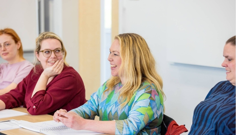 Vrouw is in gesprek en aan het lachen tijdens de cursus acute pijn service. Andere vrouw kijkt haar aan op de achtergrond.