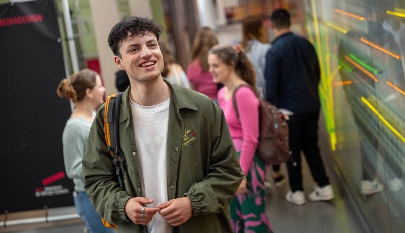 Student staat in de gang met de rugzak op de rug, in de lichtstraat van gebouw R26.