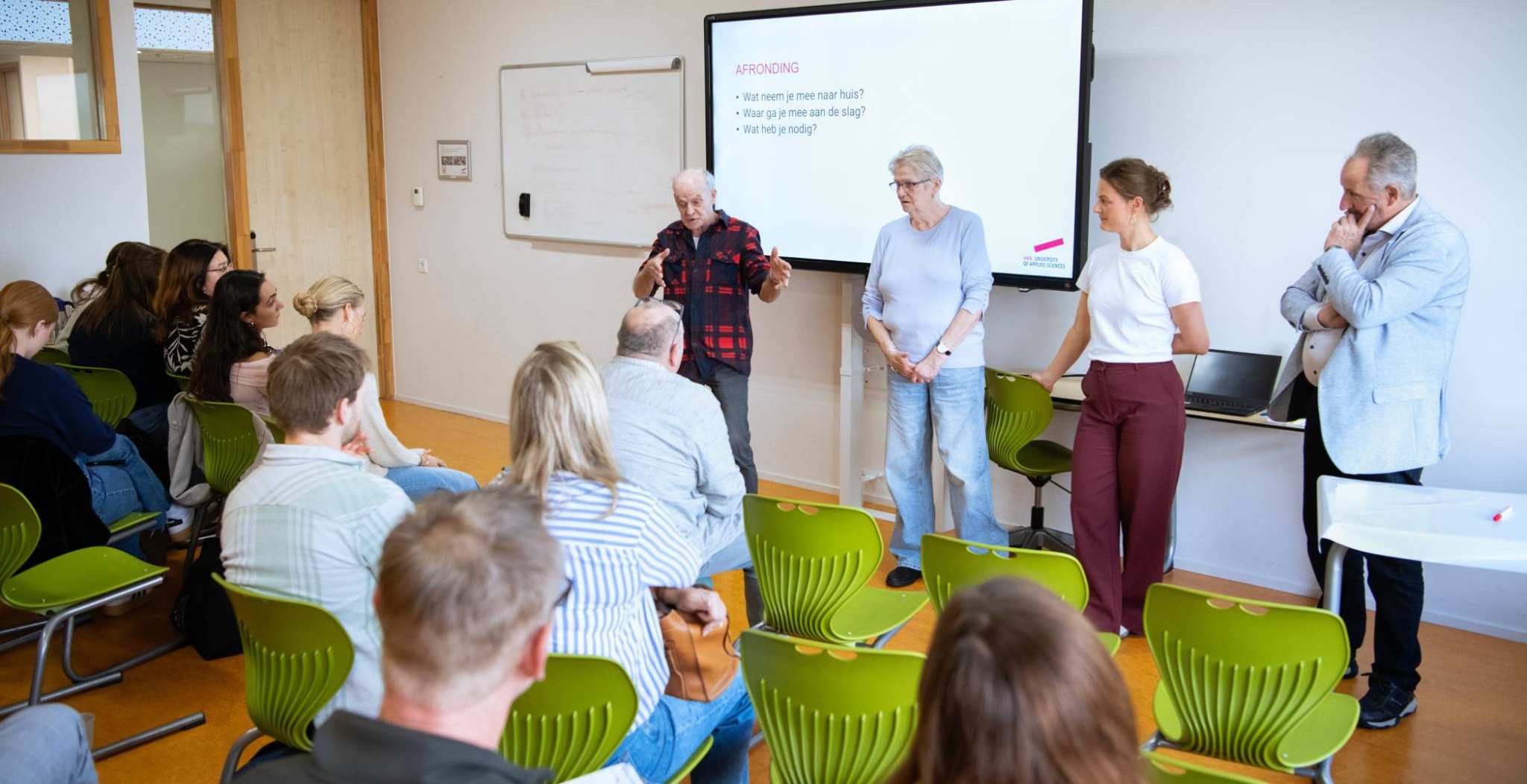 3 taalambassadeurs vertellen hun verhaal. Michel draagt een geruite blouse met rood zwart. Anneke heeft grijs haar en draagt een blauwe top en Rob heeft een lichtblauwe blazer aan.