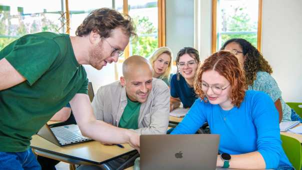 Docent wijst iets aan op de laptop van twee studenten