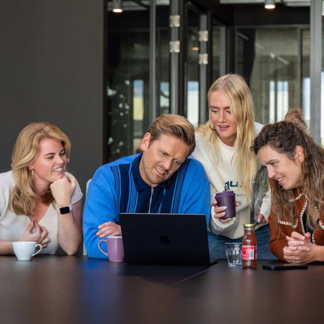 Groep studenten aan tafel kijkend naar laptop in overleg