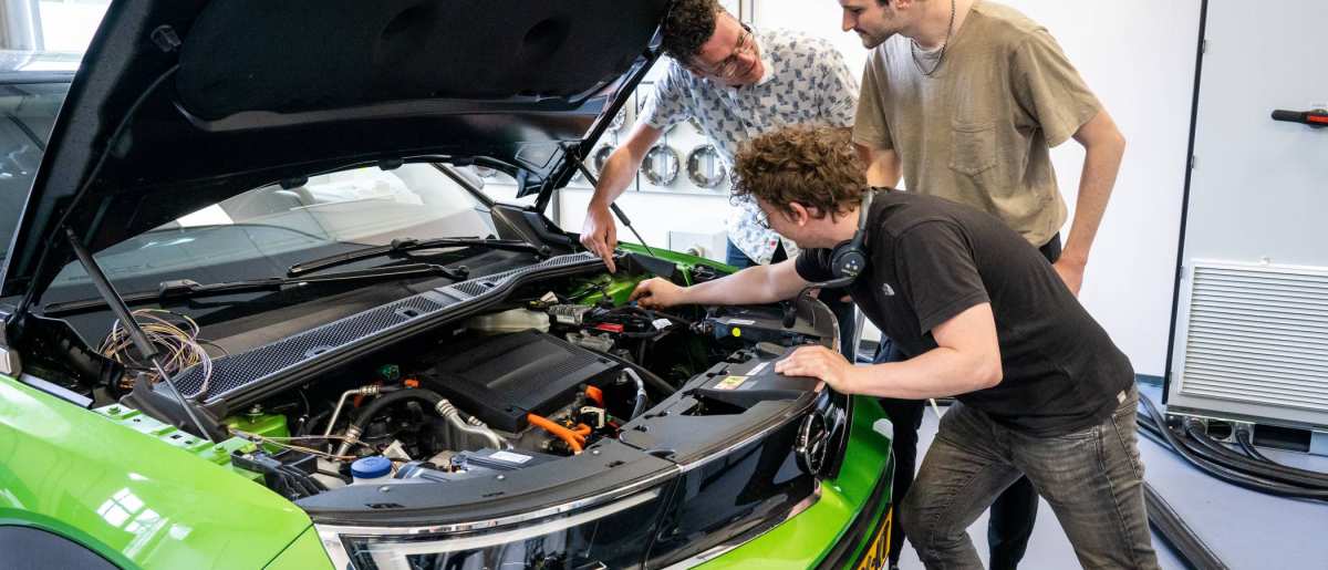 Studenten en docent automotive kijken naar de motor van de auto.