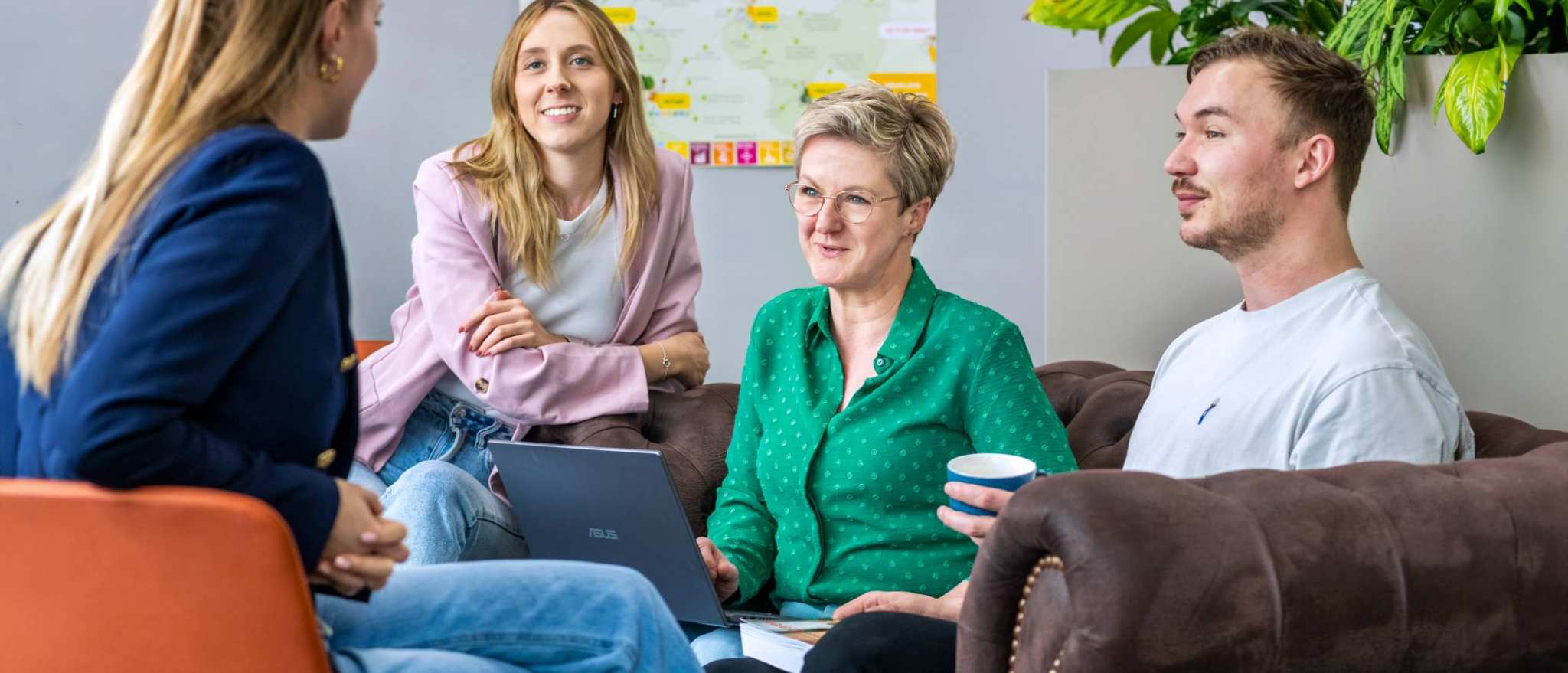 Vier studenten zitten met laptops bij elkaar en luisteren naar elkaar.