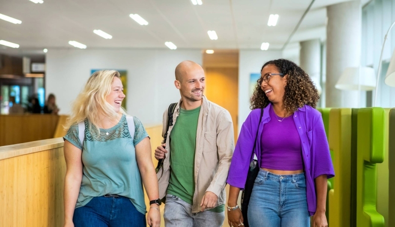 Docent wijst iets aan op de laptop van twee studenten