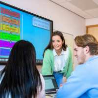 Studenten van Leraar Economie werken aan een groepsopdracht en de docent kijkt toe.