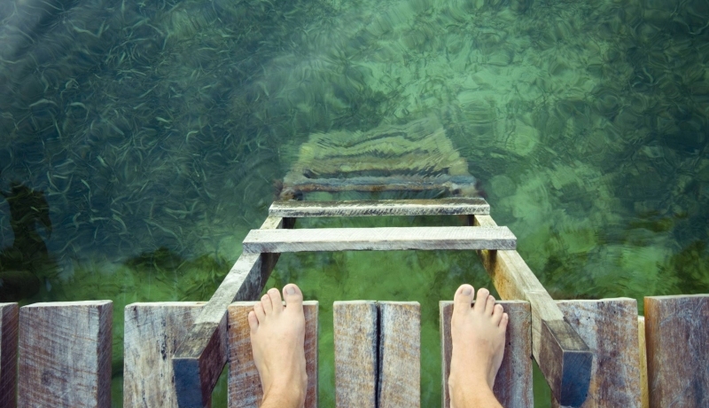 stockfoto van voeten op een vlonder aan de rand van groen water