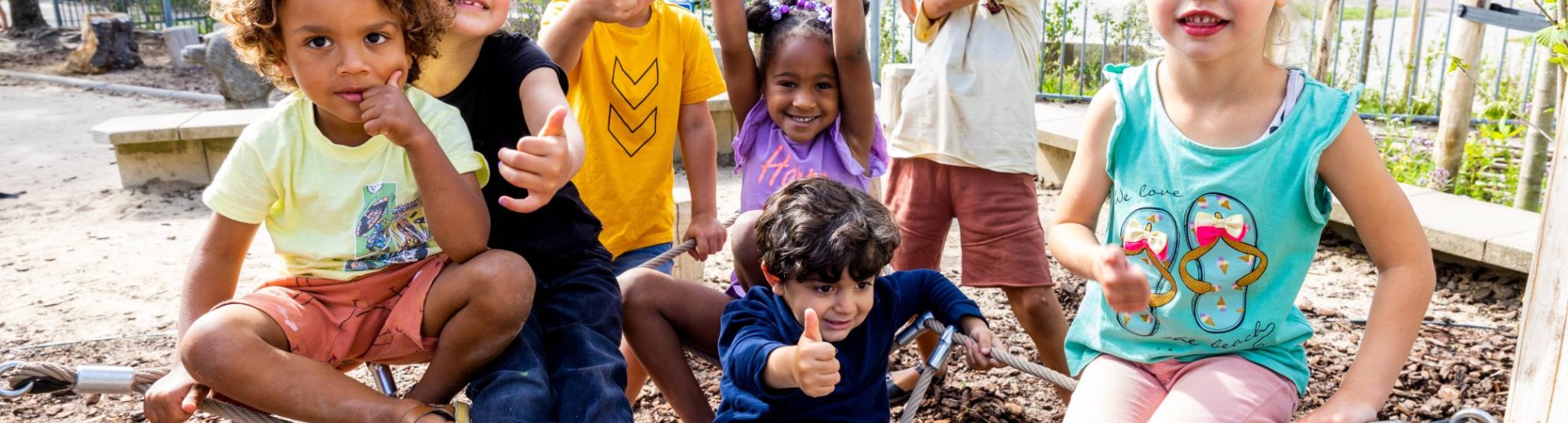 Zeven kinderen poseren buiten op het klimnet. Foto van de opleiding leraar basisonderwijs
