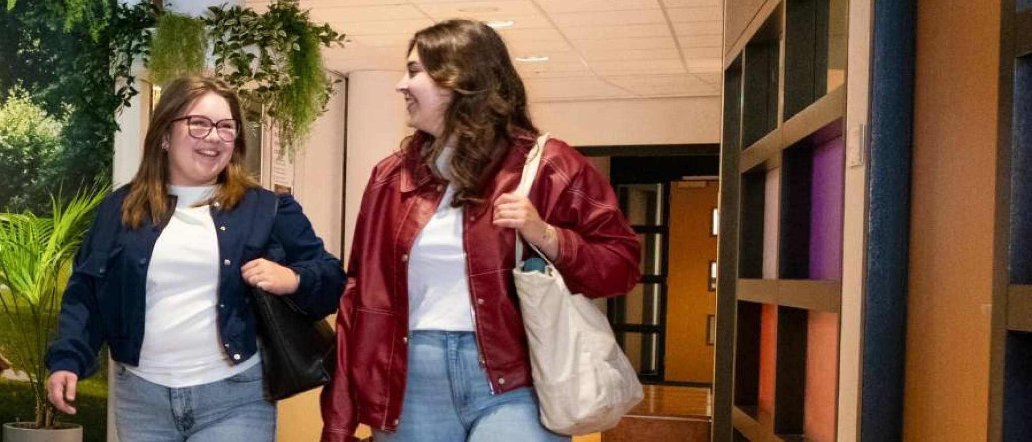 Studenten in gang bij Ergotherapie aan tafel overleggen met elkaar en 2 studenten komen in gang aanlopen. 