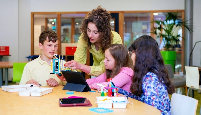Een student heeft speelgoed vast, terwijl de kinderen toekijken.