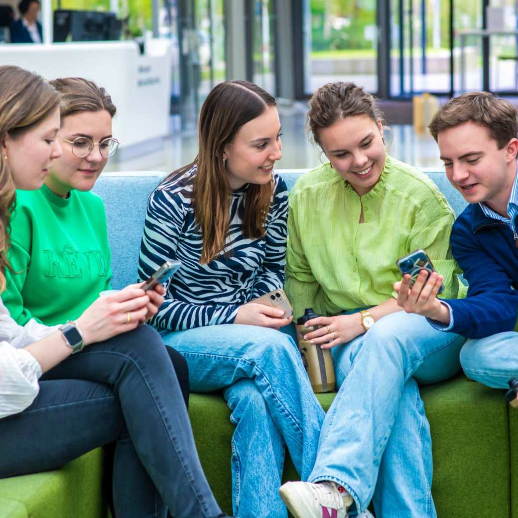 Een groep studenten zit op een groene bank samen te lachen.
