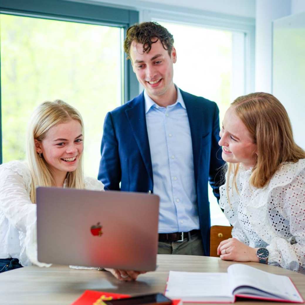 Een docent van de opleiding human resource management legt studenten iets uit aan de hand van een laptop