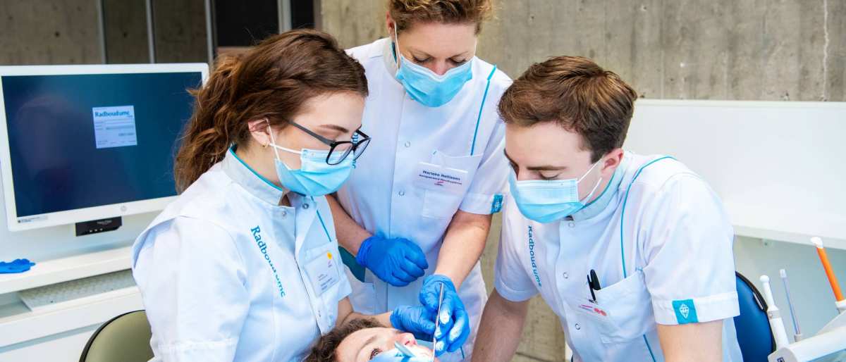 2 studenten en een docent kijken in de mond van een patient op een behandelstoel.