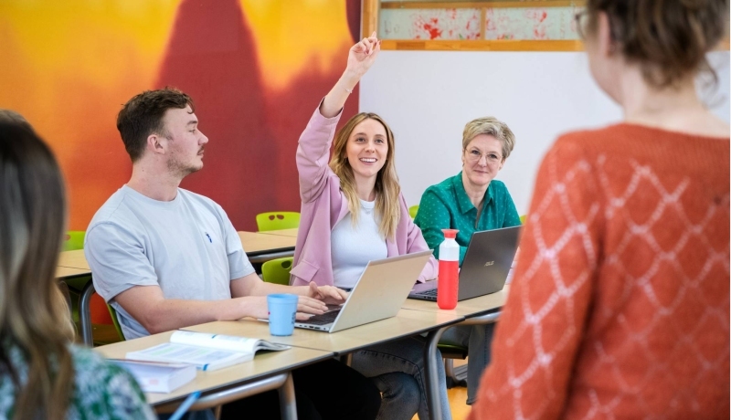 Drie master studentes zitten lachend aan tafel.