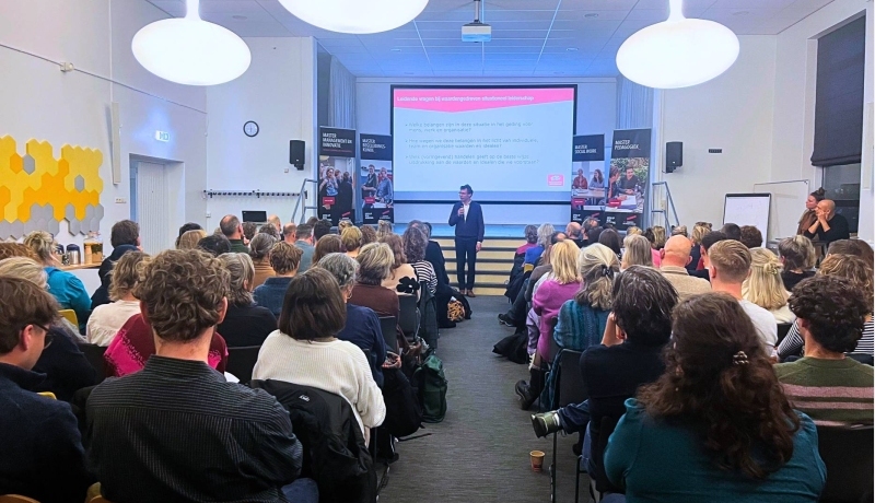 beeld van aula aan de groenewoudseweg waar deelnemers aan het kennisevent wijs leiderschap op stoelen zitten in de zaal