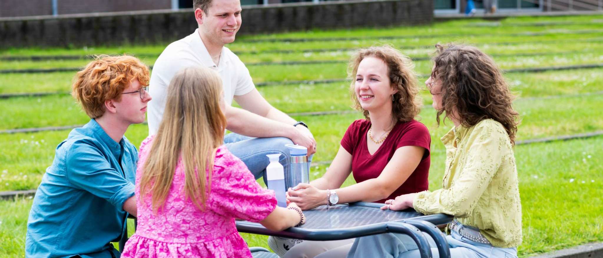 Vijf studenten zitten samen aan een tafel buiten. 