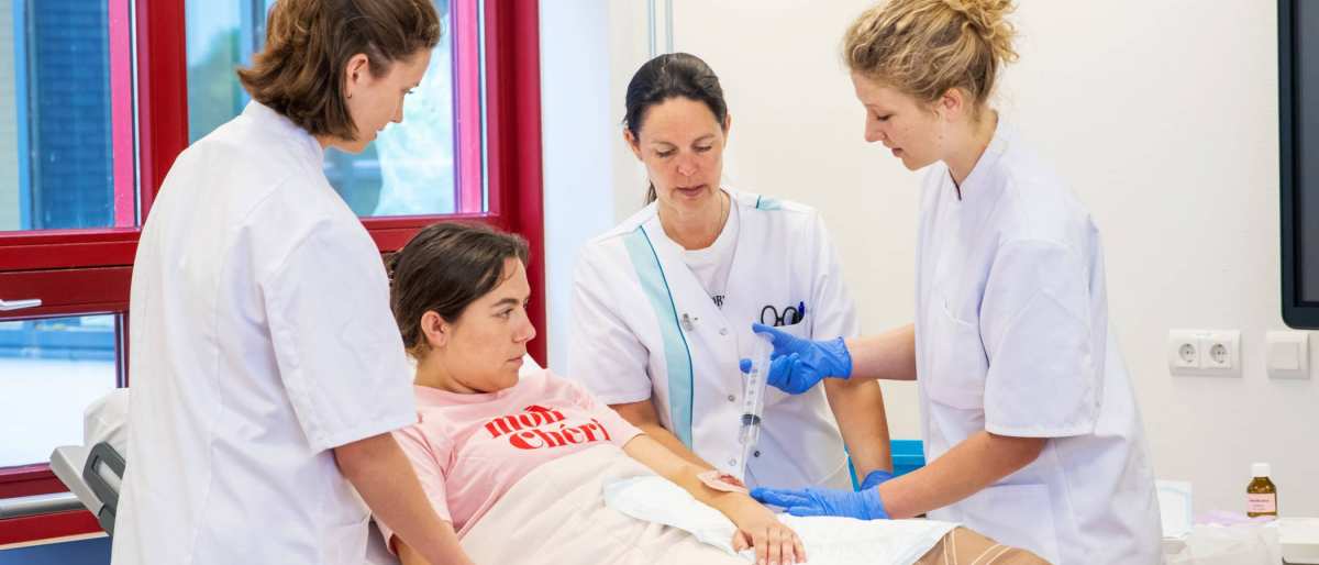 Docent kijkt mee met studenten die bezig zijn met oefenen wondverzorging
