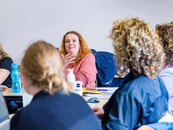 Vrouw in roze trui is in gesprek met docent tijdens de cursus acute pijn service.