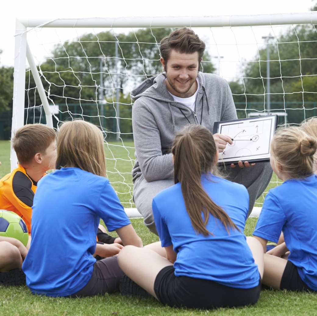 sportleraar geeft team met basisschool voetbalteam instructie