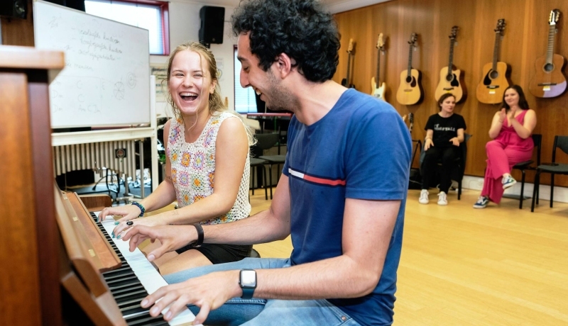 Twee studenten muziektherapie spelen samen op de piano tijdens een praktijkles