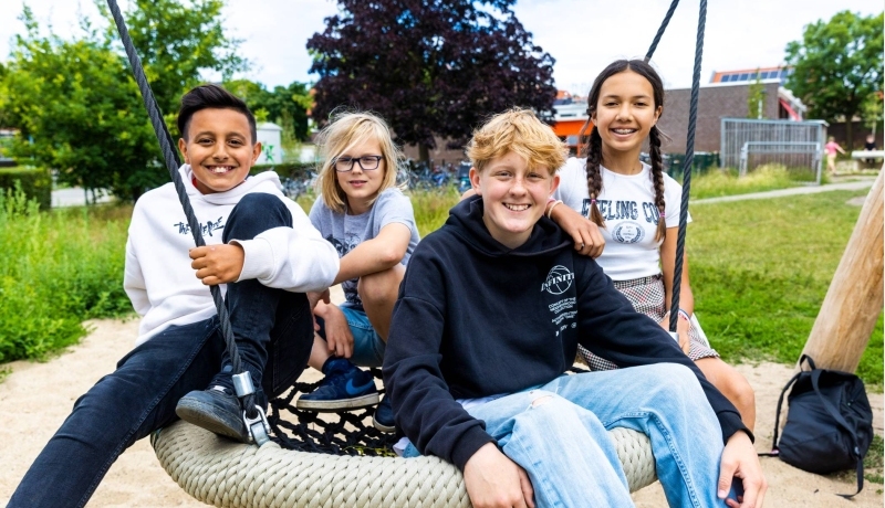 Vier leerlingen zitten buiten op een schommel. Foto van de opleiding leraar basisonderwijs 