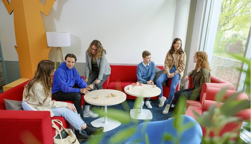 Meerdere studenten van de opleiding toegepaste psychologie aan het praten op een rode bank