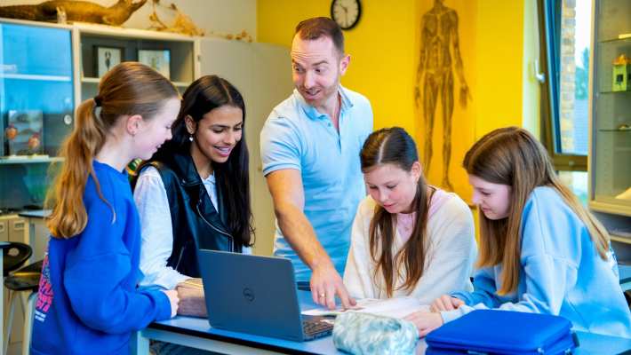 Docent Niels Janssen legt wat uit bij een laptop op tafel met 4 leerlingen op het Citadel College. 
