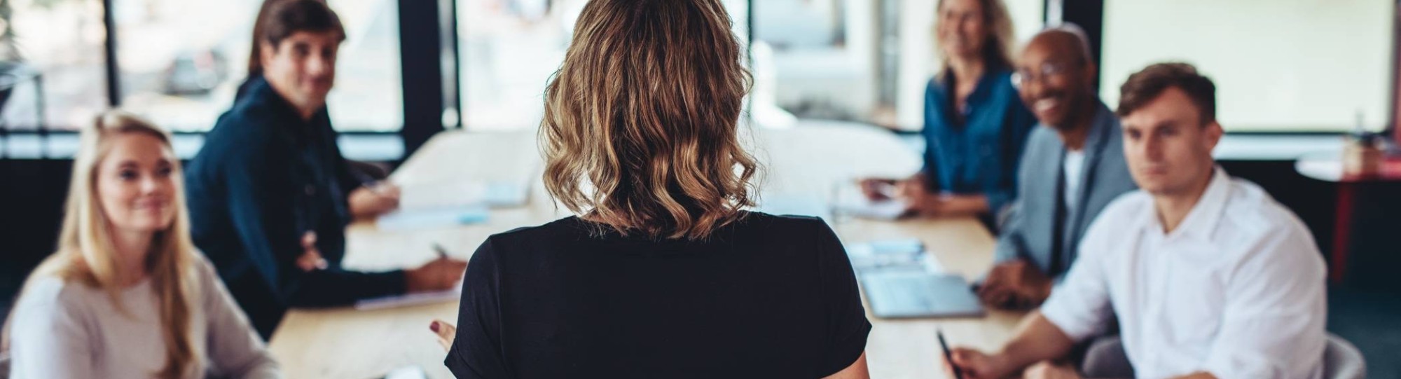 Vrouw, van achteren gezien, leidt een vergadering van een groep collega's.